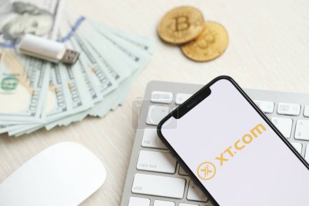 Photo for KYIV, UKRAINE - MARCH 15, 2024 XTcom logo on iPhone display screen on white keyboard with money and bitcoins. Cryptocurrency exchange portal - Royalty Free Image