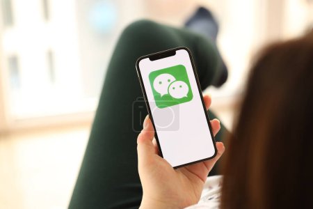 Téléchargez les photos : KYIV, UKRAINE - 1er AVRIL 2024 icône Wechat ou Weixin sur l'écran du smartphone dans les mains des jeunes femmes à l'intérieur. Femme utilisant l'application iPhone à la maison - en image libre de droit