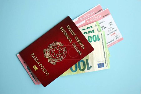 Pasaporte italiano con dinero y billetes de avión en fondo azul de cerca. Concepto de turismo y viajes