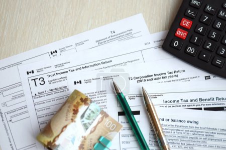 Viele leere kanadische Steuerformulare liegen auf dem Tisch, kanadische Geldscheine, Taschenrechner und Stift in Großaufnahme. Besteuerung und jährliche Buchhaltung in Kanada