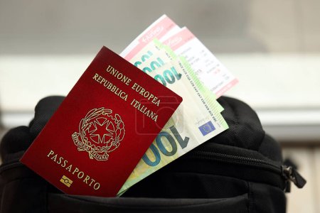 Pasaporte italiano y billetes de euro con billetes de avión en mochila de cerca
