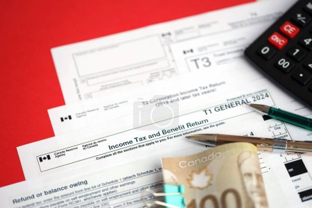 Many blank Canadian tax forms lies on table with canadian money bills, calculator and pen close up. Taxation and annual accountant paperwork in Canada