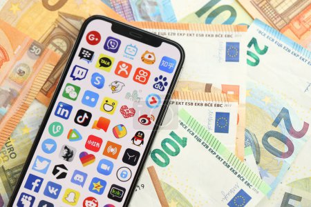 Photo for KYIV, UKRAINE - APRIL 1, 2024 Many apps icon on smartphone screen on many euro money bills. iPhone display with app logo with european currency euro banknotes - Royalty Free Image
