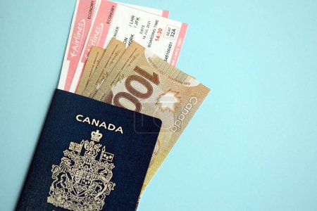 Canadian passport with money and airline tickets on blue background close up. Tourism and travel concept