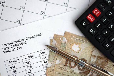 Muchos resultados de cálculo en los horarios se encuentra en la mesa con billetes canadienses, calculadora y pluma de cerca. Tributación y documentación contable anual en Canadá