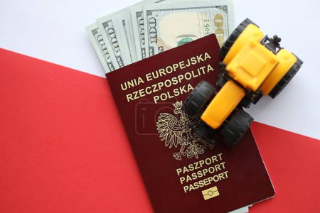 Pasaporte rojo polaco y tractor amarillo en dinero estadounidense y bandera lisa roja y blanca de Polonia de cerca