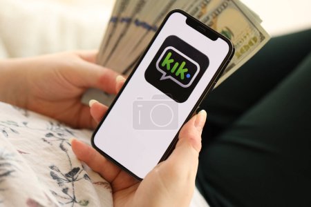 Photo for KYIV, UKRAINE - APRIL 1, 2024 Kik messenger icon on smartphone screen and money in female hand. iPhone display with app logo and hundred dollar bills in girls hands close up - Royalty Free Image