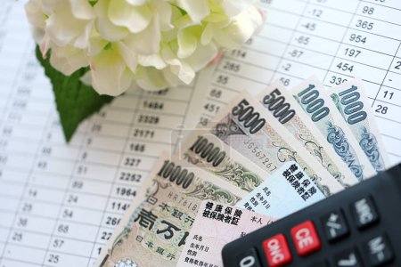 Hellblaue und rote Japan-Krankenversicherungskarten auf dem Tisch mit japanischem Yen-Geld und Taschenrechner in Großaufnahme