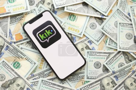 Photo for KYIV, UKRAINE - APRIL 1, 2024 Kik messenger icon on smartphone screen and many usd money bills. iPhone display with app logo and lot of hundred dollars banknotes close up - Royalty Free Image
