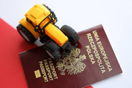Pasaporte rojo polaco y tractor amarillo sobre bandera lisa roja y blanca de Polonia de cerca