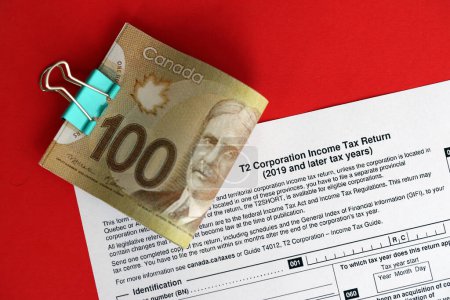 Kanadische T2-Steuerformular Körperschaftssteuererklärung liegt auf dem Tisch mit kanadischen Geldscheinen in Großaufnahme. Besteuerung und jährliche Buchhaltung in Kanada
