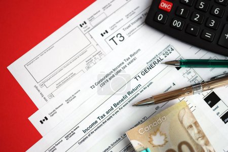 Muchos formularios de impuestos canadienses en blanco se encuentran en la mesa con billetes canadienses, calculadora y pluma de cerca. Tributación y documentación contable anual en Canadá
