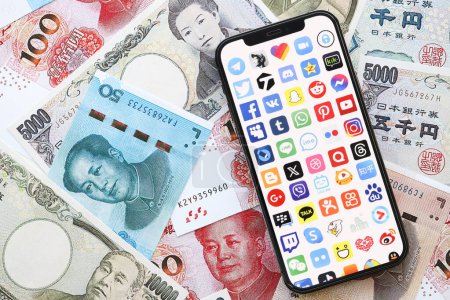 Photo for KYIV, UKRAINE - APRIL 1, 2024 Many apps icon on smartphone screen on many asian money bills. iPhone display with app logo with japanese yen and chinese yuan banknotes - Royalty Free Image