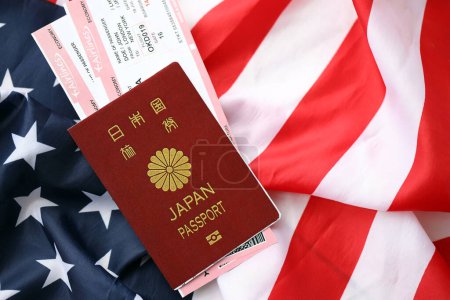Pasaporte de Japón con pasajes aéreos en bandera estadounidense de cerca. Concepto de turismo y viajes