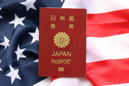Japanischer Pass auf dem Hintergrund der Nationalflagge der Vereinigten Staaten aus nächster Nähe. Tourismus- und Diplomatie-Konzept