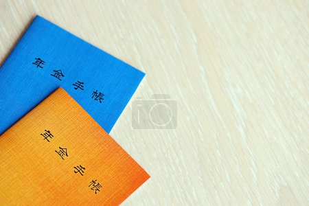 Folletos del seguro de pensiones japonés en la mesa. Libro de pensiones azul y naranja para los pensionistas japoneses de cerca
