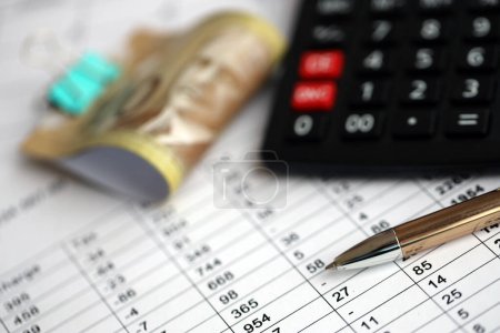 Viele Berechnungen führen zu Zeitplänen, die mit kanadischen Geldscheinen, Taschenrechner und Stift in Großaufnahme auf dem Tisch liegen. Besteuerung und jährliche Buchhaltung in Kanada