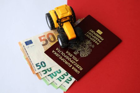 Photo for Red polish passport and yellow tractor on euro money and smooth red and white flag of Poland close up - Royalty Free Image