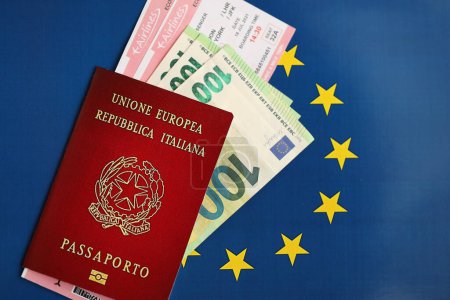 Italian passport of European Union and airlines tickets on blue flag background close up. Tourism and travel concept
