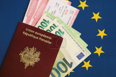 French passport of European Union and airlines tickets with money on blue flag background close up. Tourism and travel concept