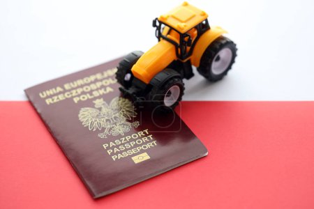 Pasaporte rojo polaco y tractor amarillo sobre bandera lisa roja y blanca de Polonia de cerca