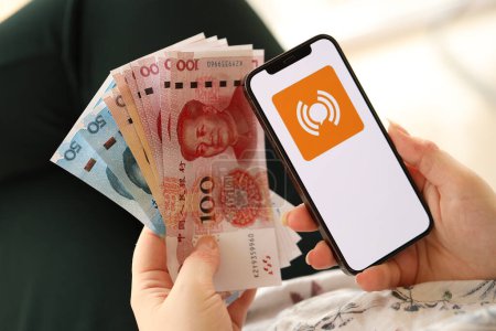 Téléchargez les photos : KYIV, UKRAINE - 1 AVRIL 2024 WeiTao icône sur l'écran du smartphone et de l'argent à la main des femmes. Écran iPhone avec logo app et billets d'argent yuan chinois dans les mains des femmes fermer - en image libre de droit