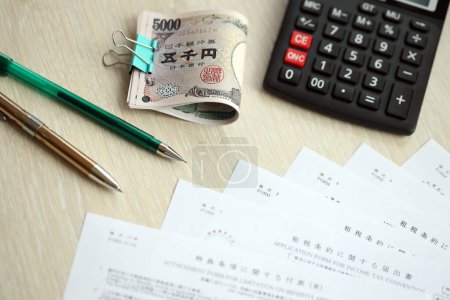 Japanese tax forms lies on table with calculator, pen and japanese yen money bills roll close up