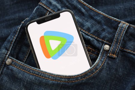 Téléchargez les photos : KYIV, UKRAINE - 1 AVRIL 2024 Tencent Video Icône WeTV sur l'écran du smartphone dans la poche du jean. Écran iPhone avec logo app cache dans la poche denims à la mode fermer - en image libre de droit