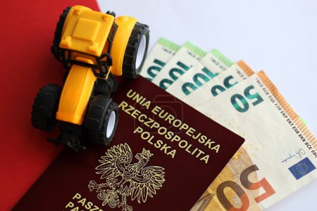 Passeport polonais rouge et tracteur jaune sur euro argent et drapeau rouge et blanc lisse de la Pologne gros plan