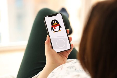 Téléchargez les photos : KYIV, UKRAINE - 1 AVRIL 2024 Tencent icône QQ sur l'écran du smartphone dans les jeunes mains féminines à l'intérieur. Femme utilisant l'application iPhone à la maison - en image libre de droit