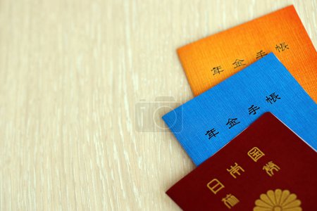 Japanische Broschüren zur Rentenversicherung auf dem Tisch mit Reisepass. Blaues und orangefarbenes Rentenbuch für japanische Rentner hautnah