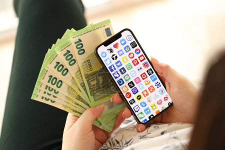 Photo for KYIV, UKRAINE - APRIL 1, 2024 Many apps icon on smartphone screen and money in female hand. iPhone display with app logo and hundred euro bills in girls hands close up - Royalty Free Image