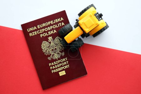 Roter polnischer Pass und gelber Traktor auf glatter rot-weißer Flagge Polens aus nächster Nähe