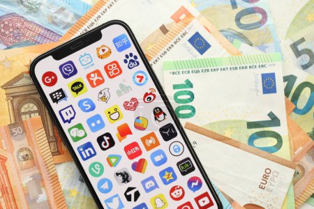 Photo for KYIV, UKRAINE - APRIL 1, 2024 Many apps icon on smartphone screen on many euro money bills. iPhone display with app logo with european currency euro banknotes - Royalty Free Image