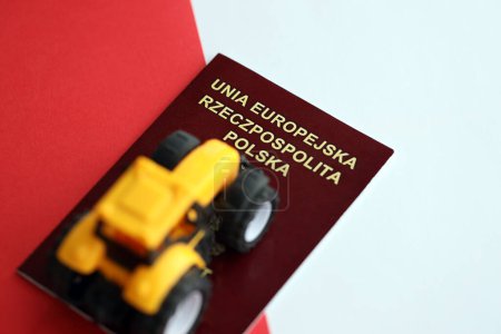 Passeport rouge poli et tracteur jaune sur drapeau rouge et blanc lisse de la Pologne gros plan