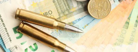 Yellow cartridges and shell casings on euro banknotes. Lot of bills of European union currency and ammo close up