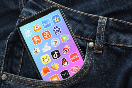 Téléchargez les photos : KYIV, UKRAINE - 1 AVRIL 2024 icône des applications asiatiques sur l'écran d'affichage du smartphone dans la poche du jean. Écran iPhone avec logo app cache dans la poche denims à la mode fermer - en image libre de droit