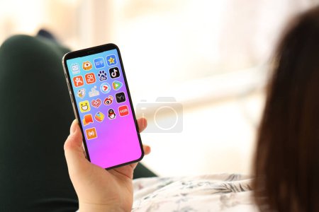 Téléchargez les photos : KYIV, UKRAINE - 1 AVRIL 2024 icône des applications asiatiques sur l'écran du smartphone dans les mains des jeunes femmes à l'intérieur. Femme utilisant l'application iPhone à la maison - en image libre de droit