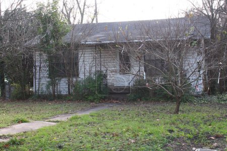 White, distressed house surrounded by shrubbery in any neighborhood in The United States.