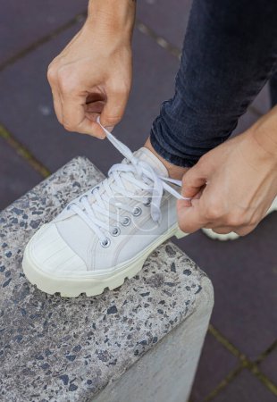 Photo for Girl in white sneakers and black jeans tying her shoelaces - Royalty Free Image