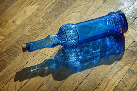 Photo for A blue glass bottle lying on the ground pierced by the rays of the sun - Royalty Free Image