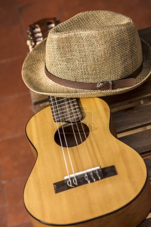 Photo for A guitar resting on a wooden box and a straw hat and clay flooring - Royalty Free Image
