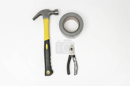 Foto de Un par de alicates, un rollo de cinta adhesiva gris y un martillo de carpintero sobre una superficie blanca - Imagen libre de derechos