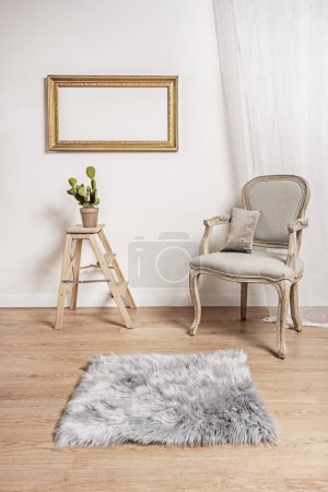 ein unlackierter heller Holzsessel mit grauem Polstersitz, eine dreistufige Holzleiter mit Pflanze, helle Holzböden und ein Paar vergoldete Holzrahmen an der Wand
