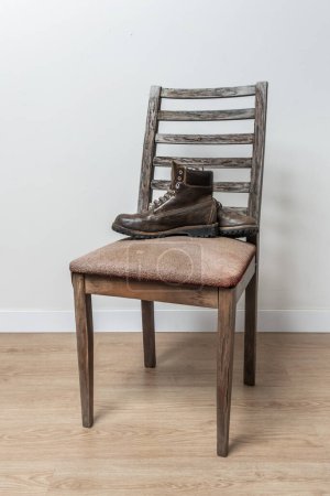 Foto de Un par de botas de cuero marrones de triple costura en una silla vieja en una habitación con suelos de parquet marrón y paredes blancas - Imagen libre de derechos