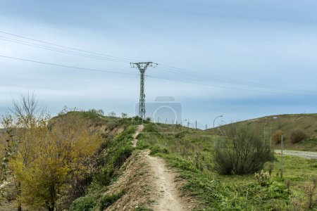 A narrow mountain bike trail up a small slope to a high voltage pylon