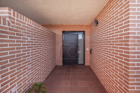 Access porch to a single-family home with metal door and terracotta-colored brick walls