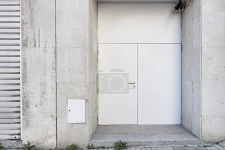 Gray access door to a ground floor premises with a security lock on a white cement facade  