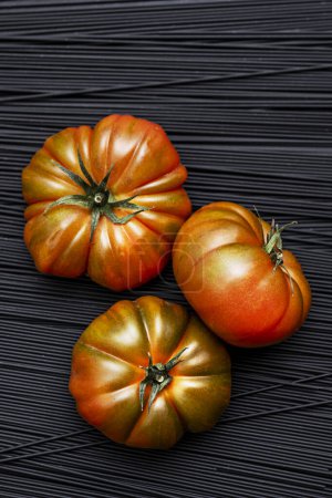 Ein Trio saftig reifer Raf-Tomaten auf einem Hügel schwarzer Nudeln