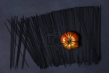 Eine saftige reife Raf-Tomate auf schwarz gefärbten Spaghetti auf einer glatten schwarzen Oberfläche